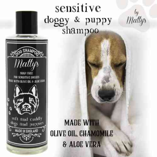 A bottle of Matty's sensitive doggy and puppy shampoo is displayed next to a relaxed puppy wrapped in a white towel. The bottle label indicates it is soap-free and made with olive oil, chamomile, and aloe vera, and is designed for soft and cuddly dogs and puppies.