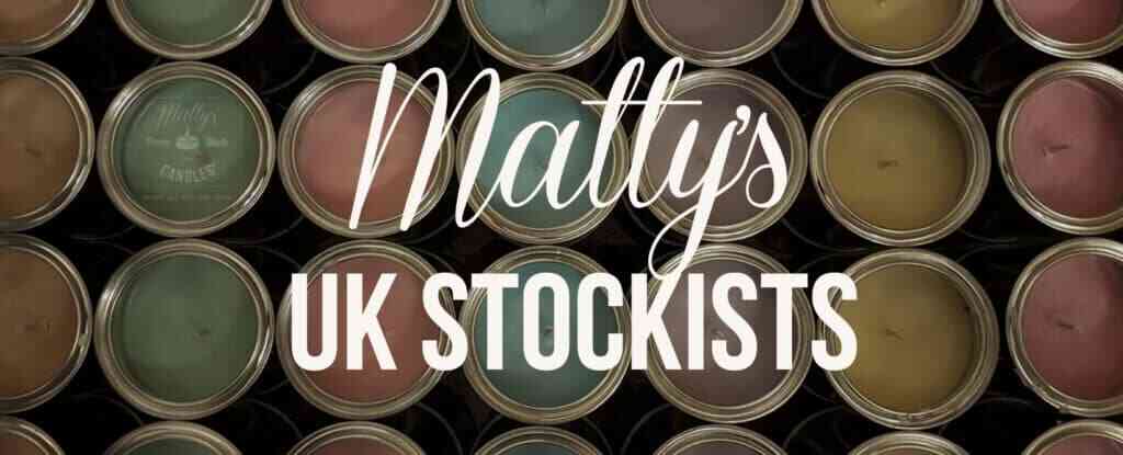 A display of multiple colored candles in metal tins, stacked in rows. Over the image, the text in white reads: "Matty's UK STOCKISTS." The candles, supplied by various stockists, vary in colors including shades of green, pink, yellow, and blue.