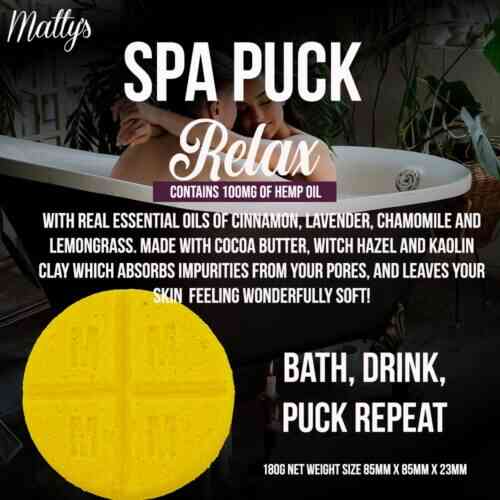 Image of a 100mg Relax Spa Puck product packaging. The box features text about the product's ingredients, including cinnamon, lavender, chamomile, and lemongrass essential oils, and hemp oil. The text also mentions the puck can be used in baths. A bright yellow puck is pictured.