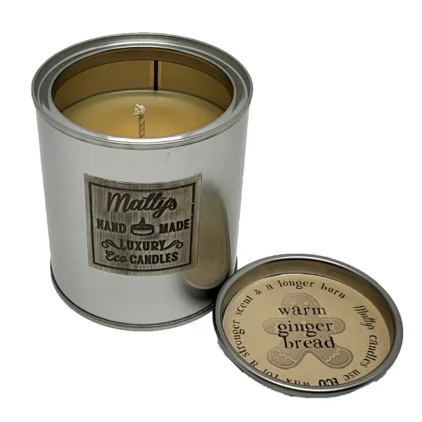 A silver tin "Gingerbread Scented Candle" by Matty's Handmade Luxury Eco Candles sits with the lid off, revealing the wick. The lid notes “warm gingerbread,” plus a stronger scent and longer burn time.